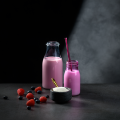 Pink smoothie in a glass bottle with berries on a dark background